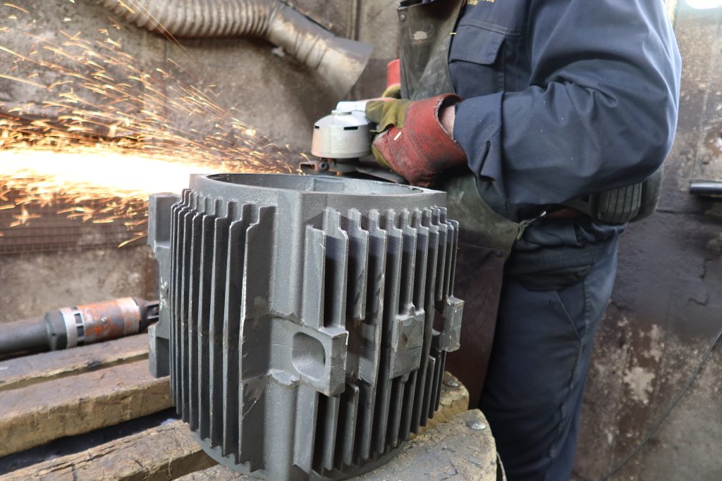 Engineer grinding electric motor housing casting in foundry