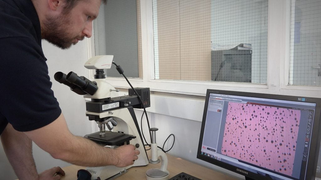 Engineer inspecting metal casting sample under microscope